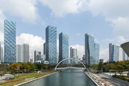 파란 하늘 아래 늘어선 송도의 유리 고층 빌딩과 센트럴파크 수로를 가로지르는 아치형 보행교