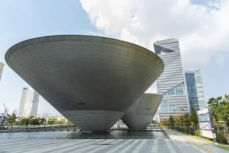 물 위에 놓인 그릇을 뒤집은 듯한 곡면 형태의 트라이보울과 뒤로 보이는 송도 빌딩숲