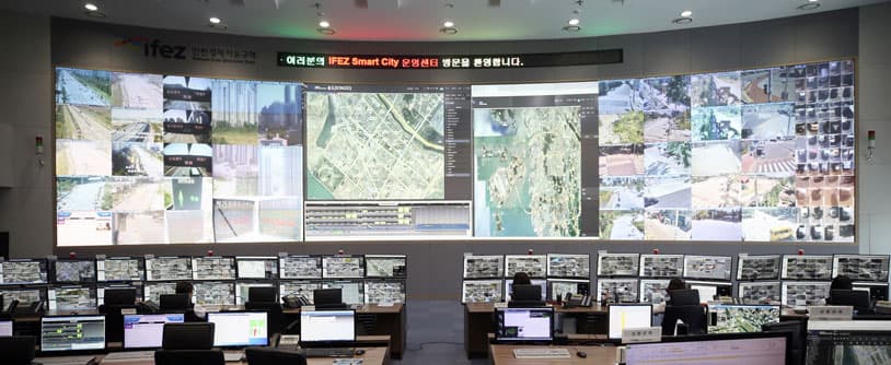 다수의 CCTV 화면과 지도가 표시된 대형 영상벽 앞에서 관제 요원들이 근무하는 IFEZ 스마트시티 통합운영센터